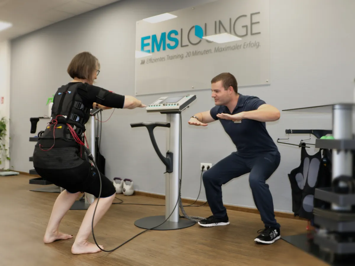Manu trainiert in der EMS Lounge Leverkusen mit einer Kundin, beide machen eine Kniebeuge